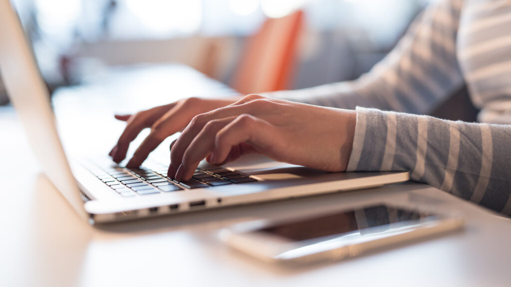 A young woman typing on a laptop in an office space.