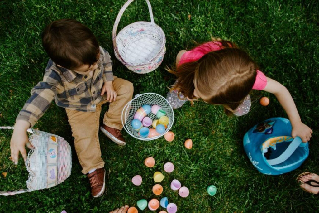 Two children sitting on some grass with Easter eggs and baskets.