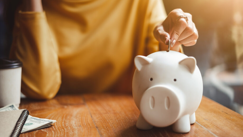 A woman placing a coin in a piggy bank.