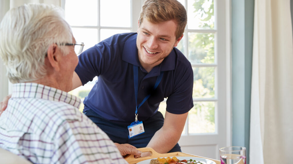 A care worker serving an older man dinner.