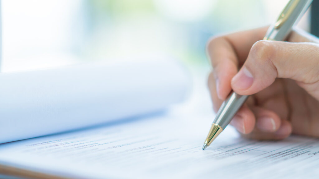 A hand holding a pen and marking paperwork.