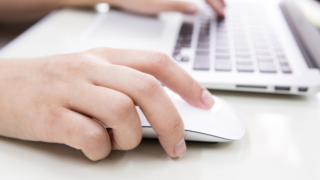 A person typing on a laptop keyboard and using a mouse.