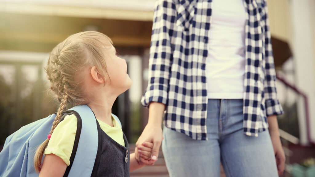 A mother and daughter holding hands as they walk to school.