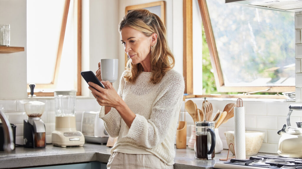 A woman drinking a coffee while looking at her phone.