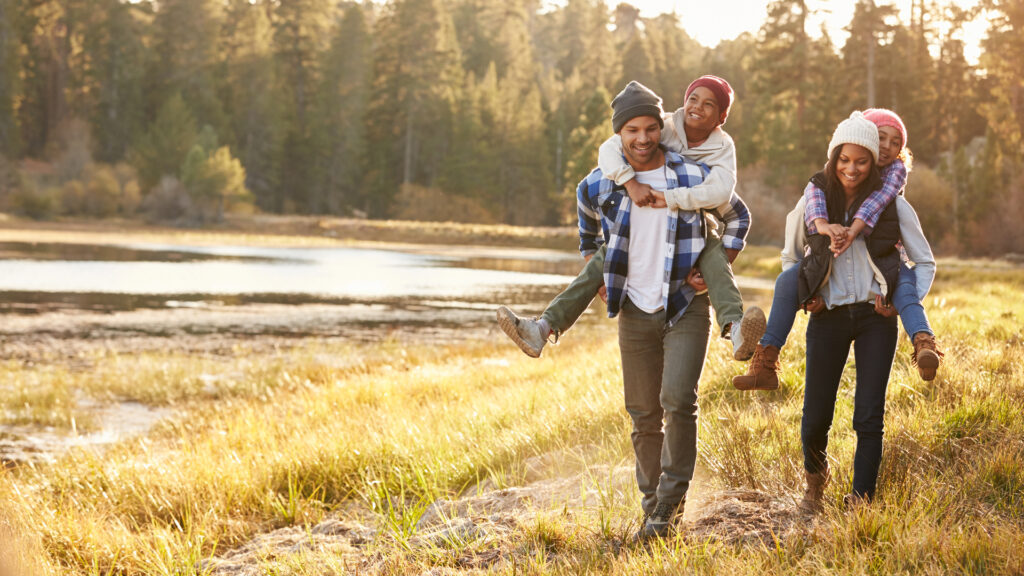 Parents walking through a park giving children a piggyback ride.