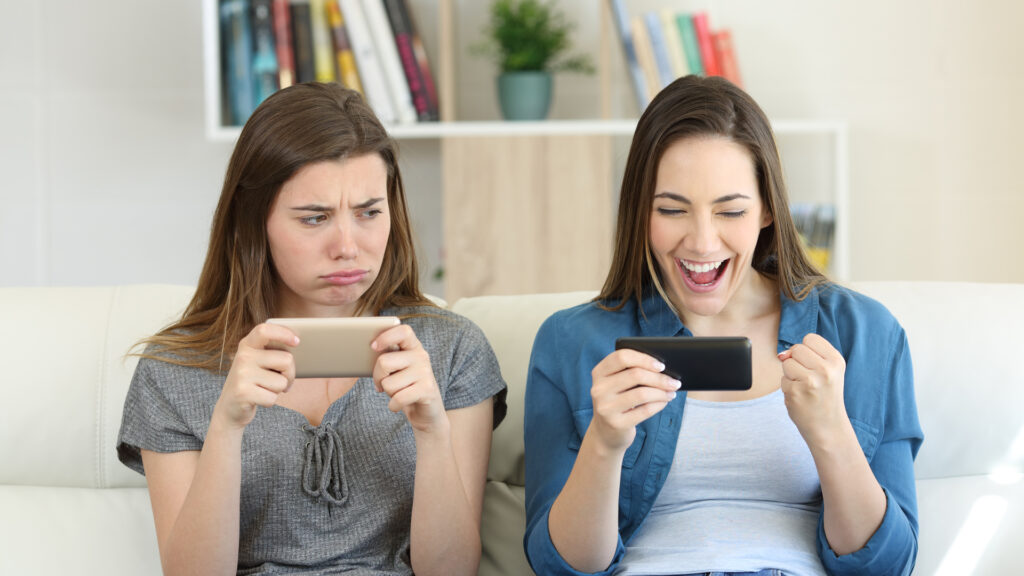 one girl looking envious at the delighted girl next to her on the sofa