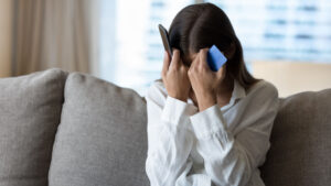 A woman holds her head with a phone in one hand and a bank card in the other.