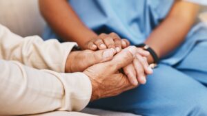 An elderly person holding hands with a nurse.